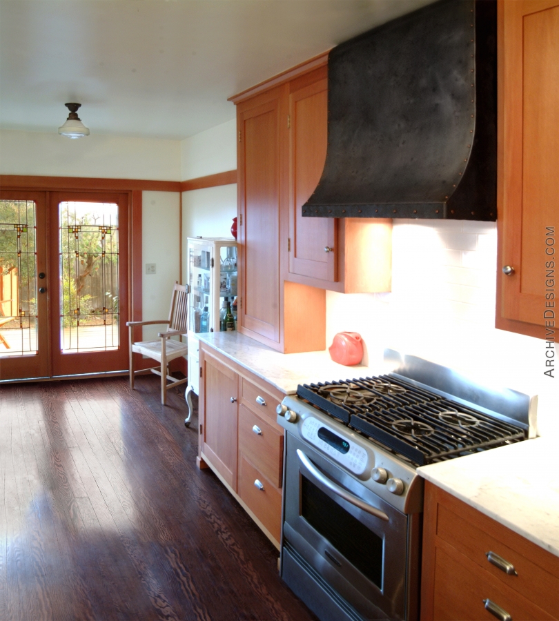A distressed steel hood with dome head copper rivets helps anchor a pleasant California bungalow kitchen, by Archive Designs.